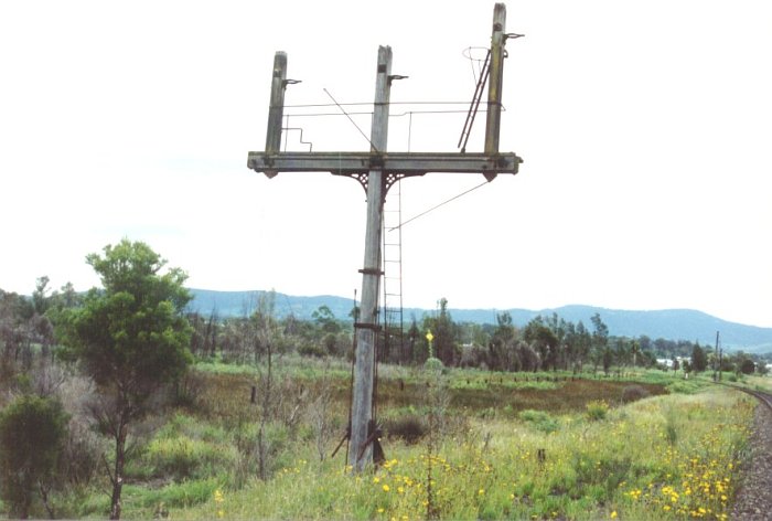 The distinctive 3 arm signal that once stood on the mainline to Cessnock at Bellbird Junction & showed the settings of the various junctions at this location. The gap between the signal post & the surviving line is the site of the down main which was taken out of use between Caledonia & Bellbird Junction in 1973 with the closure of the section to Cessnock and the Bellbird Junction Signal box. With the closure of the signal box the staff machine was transferred to Caledonia.

The Signal post along with all other redundant signal posts on the SMR has since been removed.