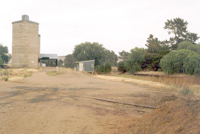 The view of the Burrumbuttock yard from the access road on the eastern side.  The remains of the platform is on the right; the Graincorp silos and weighbridge are still in use.  Although buried under soil and sand in some places, the trackwork for the remaining siding was still largely intact in 2004.
