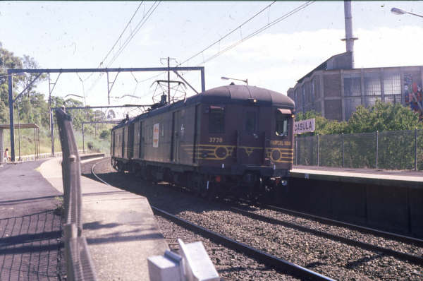 A twin set of Parcel Vans speedily run through Casula toward Campbelltown, a solitary passenger waits for the next up train.