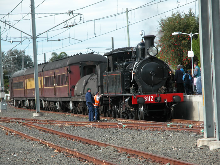 3112 and a short train stand on the back platform.