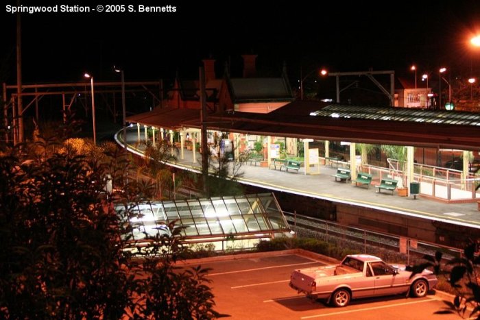 A photo of Springwood station taken after dark from the top level of the multi storey commuter carpark, looking down at Up main and platform 1.